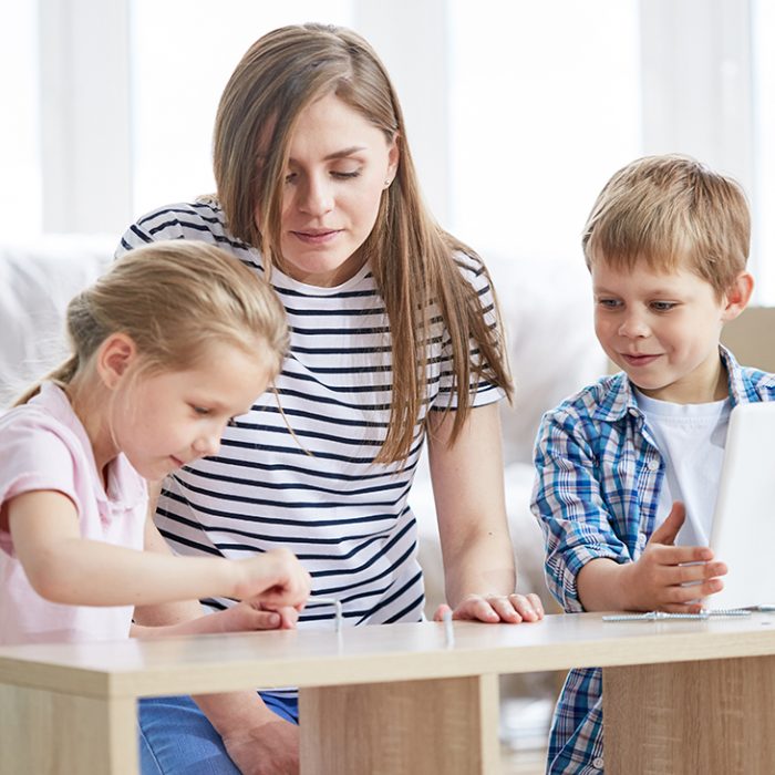 Attractive young mother and her cute children enjoying each others company while gathered together in living room and assembling furniture