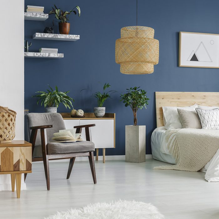 Wooden furniture and marble shelves in bedroom interior with green plants, double bed and grey armchair