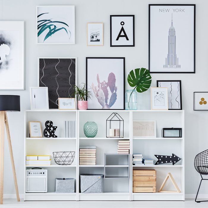 Wooden shelves with decorations, boxes and books in white living room interior with fresh plants and modern art posters