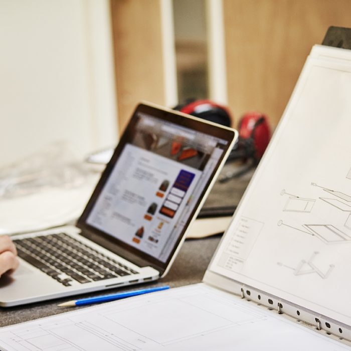 A furniture workshop making bespoke contemporary furniture pieces using traditional skills in modern design. A laptop and paper blueprints in a file.