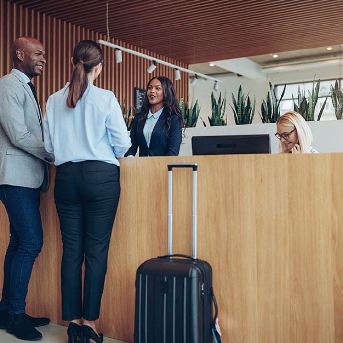 Two smiling guests talking with a concierge while checking in together at the reception counter of a hotel