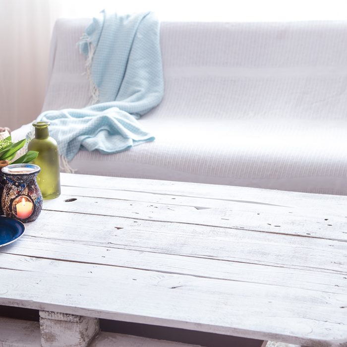 Beautiful burning candles with green leaves in purse on white wooden table